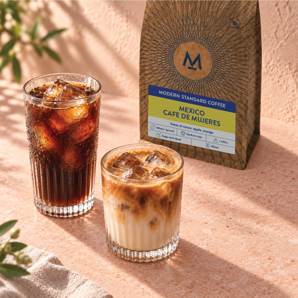 Cafe de Mujeres decaf coffee bag with iced black coffee and an iced latte