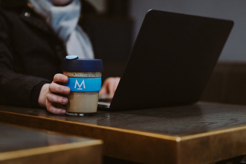 Customer working on a laptop with a Modern Standard Coffee KeepCup at Ole & Steen