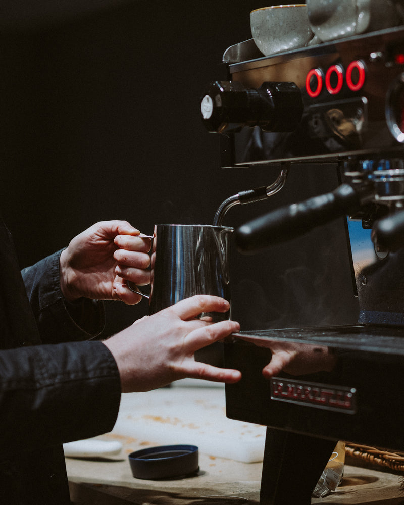 Barista handing over a milk jug at the espresso machine at Ole & Steen