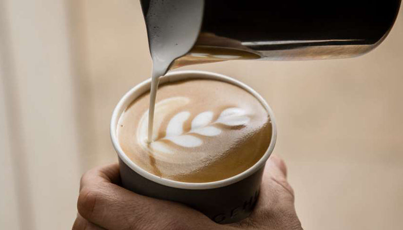 A flat white with latte art being served in a ceramic cup