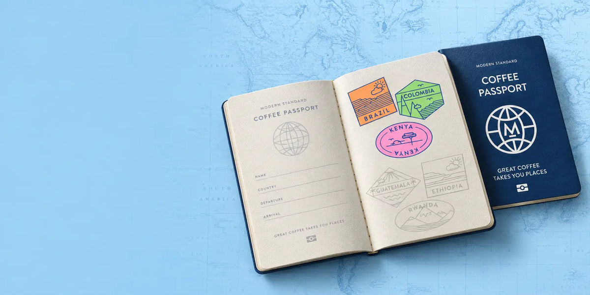A Modern Standard Coffee Passport beside an open passport stamped with Brazil, Colombia and Kenya badges, with Guatemala, Ethiopia and Rwanda still to collect, lying on a map