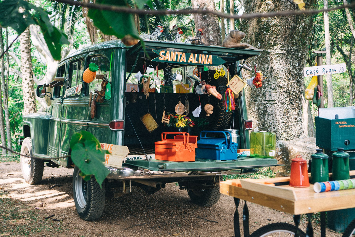 A vintage green truck set up as a coffee stand beside a table of brewing equipment under the trees