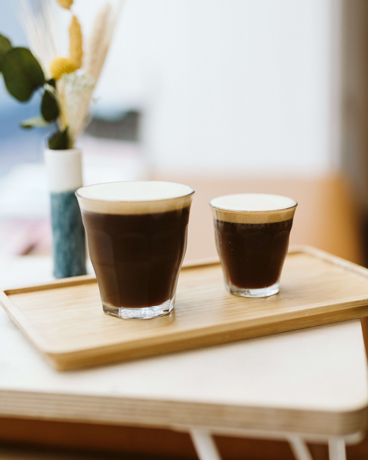 Two glasses of dark coffee on a wooden tray