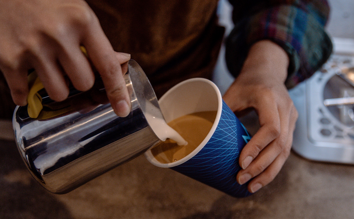 A barista pouring steamed milk into a Modern Standard cup