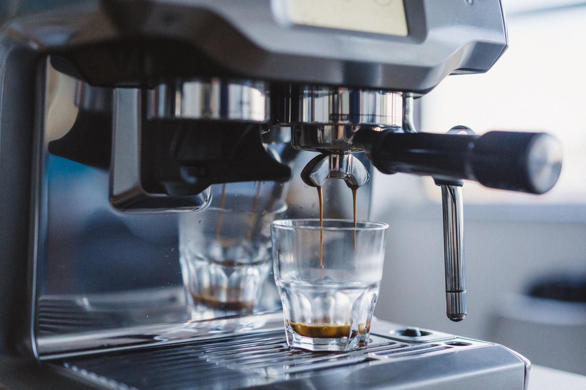 A double espresso pouring from a home espresso machine into two glasses